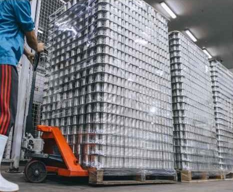 Soluciones de embalaje para la industria cervecera. Imagen de un almacenista empujando un montacarga con tarimas llenas de latas para cervezaSoluciones de embalaje para la industria cervecera.