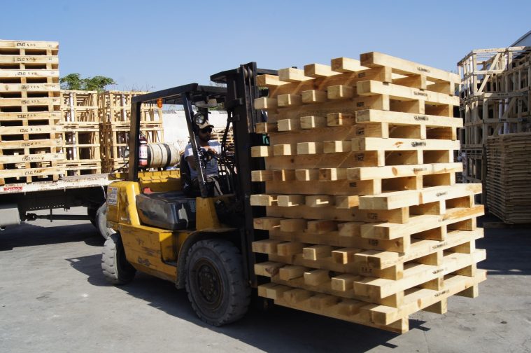 Montacargas transportando pilas de tarimas de madera en un área de carga.