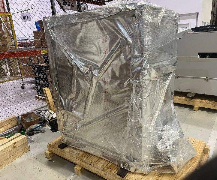 Equipo industrial envuelto en plástico, sobre un palé de madera en un entorno industrial.