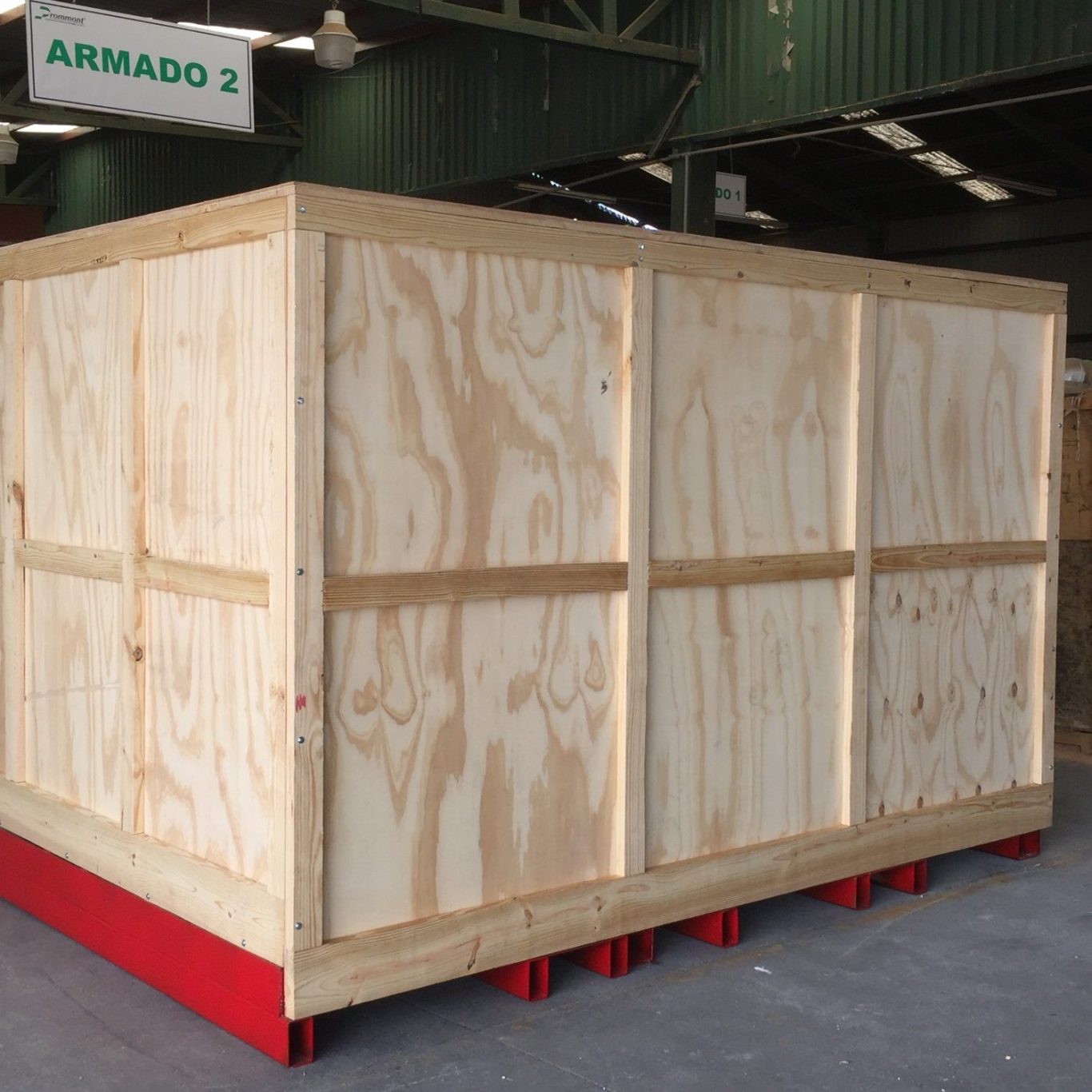Gran caja de triplay, estructurada con madera solida, de grandes con costados de paneles y base de acero rojo en un entorno industrial.