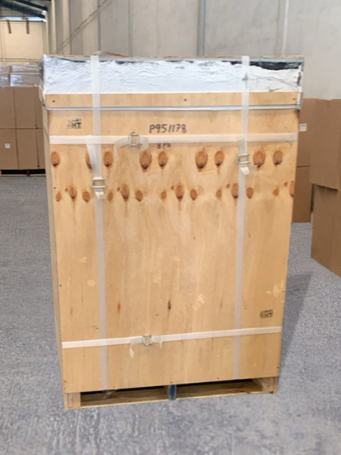 Caja de madera con tapa asegurada y correas, ubicada en un entorno industrial.