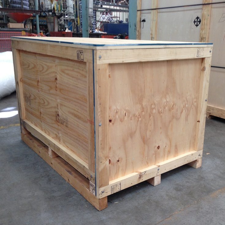 Imagen de una resistente caja de triplay estructurada con madera solida y fleje metálico, sobre el piso de una fábrica.