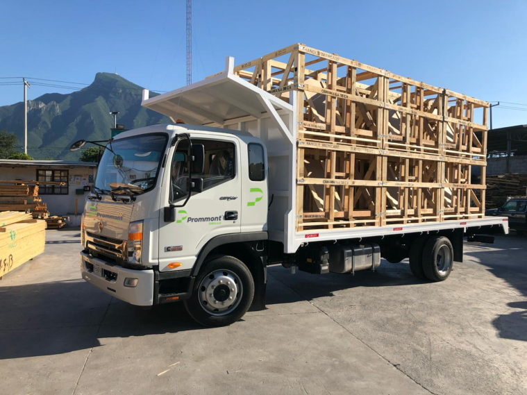 Logística Prommont: entrega de huacales al cliente Camión de repartición, blanco con logotipo de marca Prommont, cargado de estructuras de madera para un cliente, montañas al fondo.