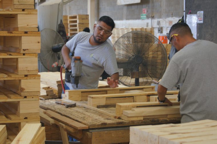 Hombres trabajando en una fábrica, usando herramientas en piezas de madera.